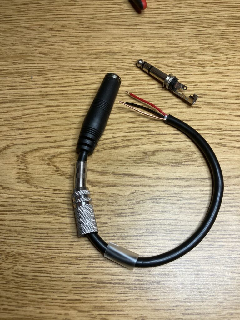 Image of a 1/4" stereo female jack on a cord with stripped wire ends, and a 1/4" stereo male plug prepared for installation.